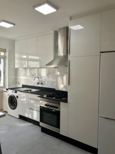Cocina moderna con muebles blancos, horno, estufa y lavadora integrada.